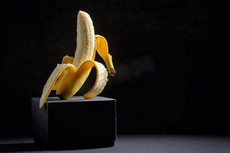 食品背景黄色摄影照片_概念与半剥皮香蕉在黑色背景