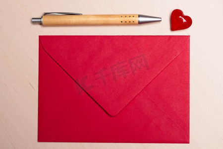 小心讨好摄影照片_红色空白信封小心和笔在木表面。情人节卡片，爱情或婚礼问候概念。