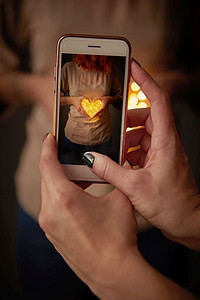 妇女在电话上拍照的女孩与圣诞灯在心脏的形状。女孩使照片在手机上