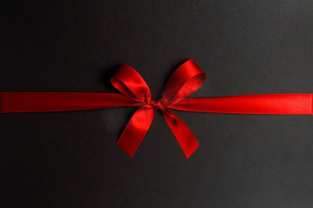 周年庆红金摄影照片_闪亮的红缎丝带和蝴蝶结在黑色背景。节日礼物的概念。闪亮的红缎丝带蝴蝶结