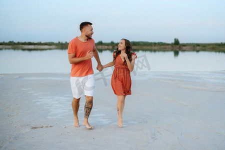 一对穿着橙色衣服的年轻夫妇带着狗在空荡荡的沙滩上