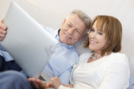 微笑的成熟夫妇在家里的卧室里使用笔记本电脑