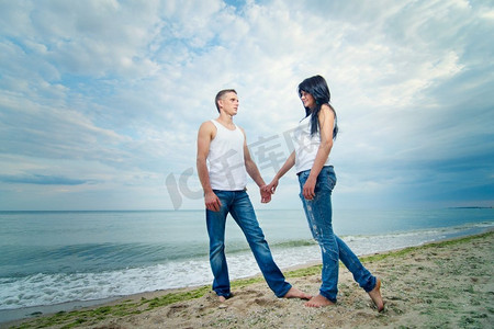 t恤女摄影照片_穿着牛仔裤和白色T恤的一男一女在海边