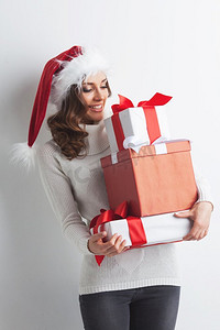 戴着圣诞帽的快乐女人，手里拿着一堆圣诞礼物。带着一大堆礼物的女人