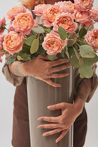 一个女孩手里拿着一个花瓶。花瓶里有一束粉红色的玫瑰，母亲节，鲜花店的概念。拿着花瓶和一束玫瑰花的女孩