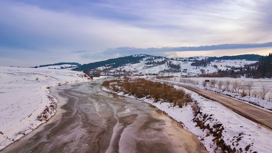 冰冻的冬季河流。从空中俯瞰白雪覆盖的村庄和道路。初春的冰雪融化。