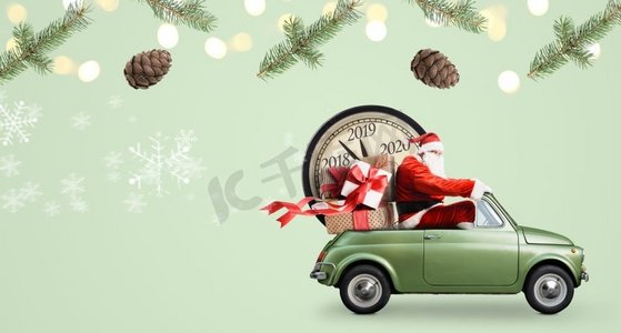 圣诞节到了摄影照片_圣诞节倒计时到了。在绿色背景下，圣诞老人在车上送新年礼物和时钟。汽车上的圣诞老人倒计时