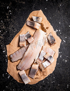 盐腌鲱鱼片放在纸上撒盐。在黑色背景上。高质量的照片。盐腌鲱鱼片放在纸上撒盐。