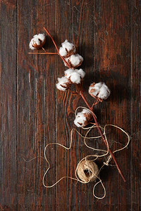 一团线团和一枝蓬松的白色棉花花放在一张棕色的旧木桌上。白色棉花花的树枝