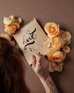 年轻女子用画笔书写情词的背影。用鲜花装饰。手用画笔写情书