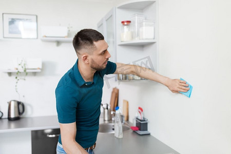 厨房挂壁摄影照片_家庭和人的概念—男人用布清洁墙壁在家庭厨房。男人用抹布清洁墙壁在家庭厨房