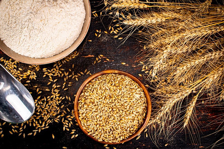 小麦粒摄影照片_面粉和小麦粒一碗放在桌子上.在黑暗的背景下。.面粉和小麦粒一碗放在桌子上. 