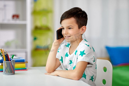 人，技术和通信概念—快乐微笑的男孩在家里打电话智能手机。快乐的男孩打电话在家里的智能手机