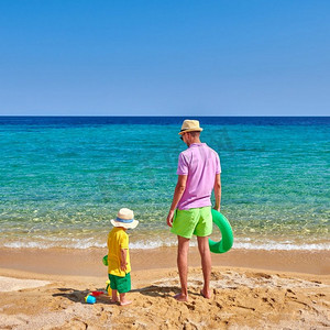 爸爸拿摄影照片_2岁的蹒跚学步的男孩在海滩上与父亲，拿着充气戒指。暑假家庭度假。希腊，西托尼亚。 