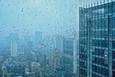 水背景摄影照片_雨水滴在窗口玻璃纹理与摩天大楼在背景。雨点落在窗户上