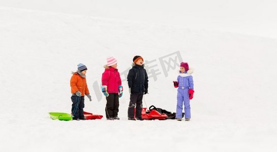 赛季摄影照片_童年，雪橇和季节概念—一群快乐的小孩子在冬天雪橇。快乐的小孩子与雪橇在冬天