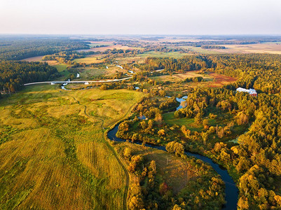 秋天农村鸟瞰图与草地，河，村庄，泥土道路和农业领域在背景。日落秋景从上面