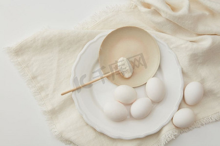 白色冲浪板摄影照片_面粉放在勺子里，鸡蛋用餐巾铺在白色的背景上，平放。鸡蛋面粉