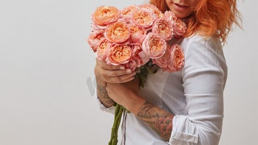 手臂上有纹身的红发女孩手捧一束粉红玫瑰,情人节,母亲节手捧花美女