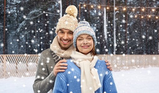 人，圣诞节和冬季假期概念—在针织帽子和围巾的愉快的夫妇在溜冰场背景快乐的夫妇在冬天的衣服