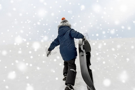 童年，雪橇和季节概念-冬天坐雪橇爬雪山的男孩。冬天的小男孩拉着雪橇爬雪山