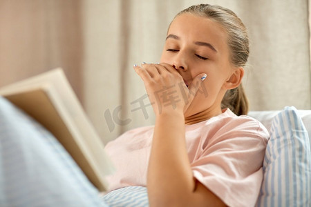 人，就寝时间和睡眠概念-打哈欠的女孩在家床上看书。打哈欠的女孩在家床上看书