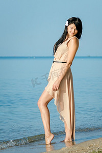 一个女孩与黑色的头发在一个米色的裙子在海岸的蓝色的大海