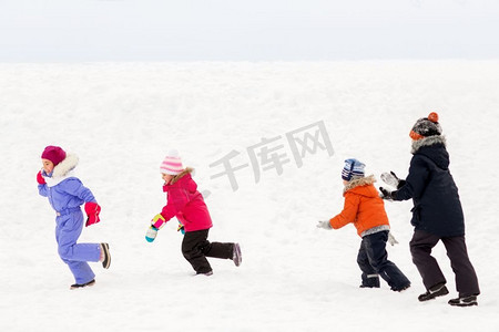 圣诞节小朋友摄影照片_童年、休闲和季节概念-一群穿着冬装的快乐小朋友在户外玩耍。冬天快乐的小孩子们在户外玩耍