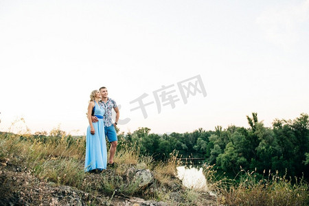 金发女孩穿着淡蓝色连衣裙，男孩在自然界的夕阳下