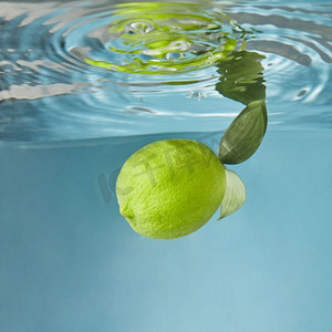 叶子水花摄影照片_新鲜的黄色柠檬，在蓝色的背景下，整个水下有绿色的叶子。黄色新鲜柠檬在蓝色背景上溅起水花