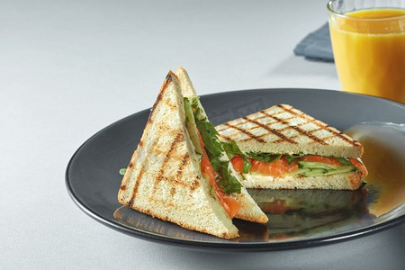 白色的桌子上放着美味的烤三明治和橙汁。盘子里的三明治