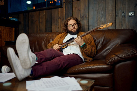 晚上坐在家里沙发上玩吉他的嬉皮士男人。创意爱好，休息和放松时间。晚上在家玩吉他的男人