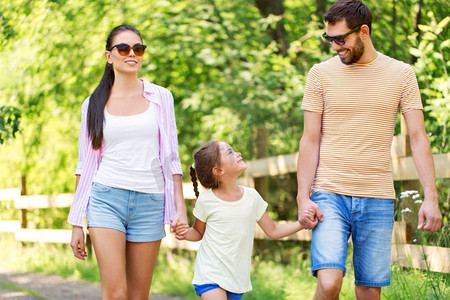 孩子散步摄影照片_家庭、休闲和人的概念-快乐的母亲，父亲和小女儿在夏令营散步。快乐的一家人在夏季公园散步