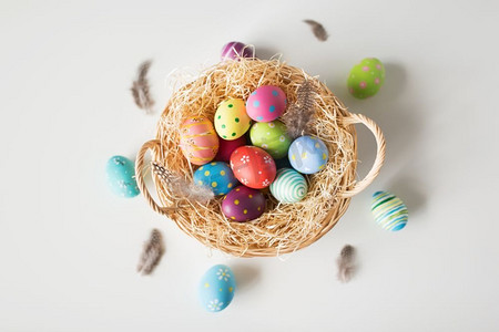 复活节，假日和传统概念—在篮子的彩色鸡蛋有稻草和鹌鹑羽毛在白色背景彩色复活节彩蛋