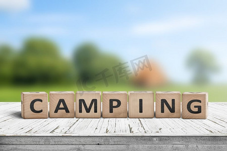 木质牌子摄影照片_夏季露营地背景模糊的木质立方体牌子上的露营字样