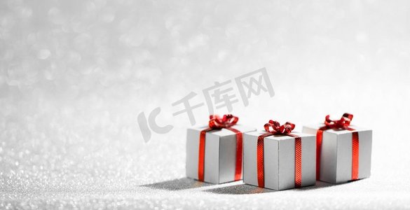 装饰礼物盒摄影照片_小装饰圣诞节礼物盒与红色丝带蝴蝶结在银闪光背景与复制空间。圣诞礼品盒上的闪光