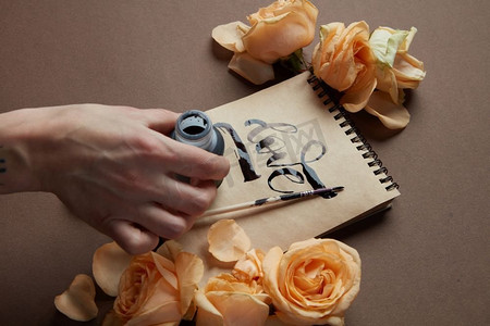 女性手写爱的字在工艺纸，玫瑰周围。手用画笔写情书