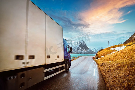 卡车在公路上的挪威峡湾日落。挪威罗弗敦群岛。移动模糊。卡车在挪威的道路上