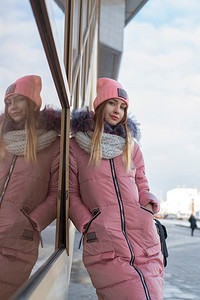 一个穿着粉色夹克的女孩在冬天走在城市里