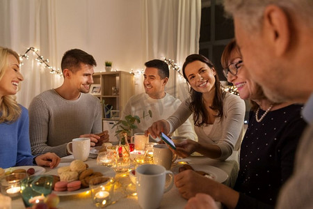 庆祝、节假日和人们概念快乐的家庭，在家里用智能手机举行茶话会。幸福的家庭在家里的茶话会上带着智能手机