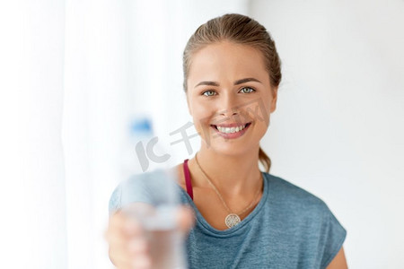 健身和健康的生活方式的概念—微笑的年轻妇女显示一瓶水。快乐的女人显示一瓶水