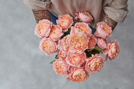 女孩的手与花束在灰色背景与复制空间美丽的粉红色玫瑰花束在妇女手中与纹身。俯视图。