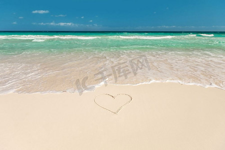 心脏蓝色背景摄影照片_浪漫度假和情人节概念—热带海滩蓝色的水和心形画在沙滩上。热带海滩与心脏在沙滩