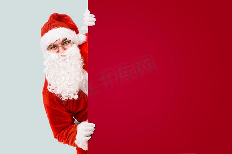 广告文案摄影照片_圣诞老人正在五颜六色的广告牌和文案版面外张望。圣诞老人和五颜六色的广告牌