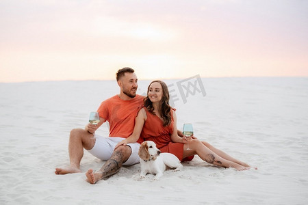 沙滩衣服摄影照片_年轻夫妇橙色衣服与狗在沙漠白色的沙滩