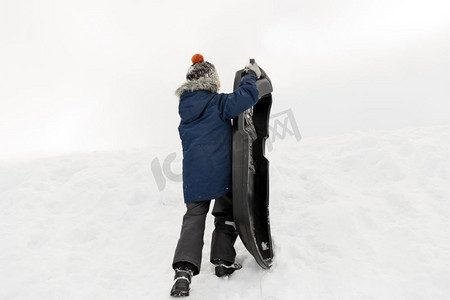 童年，雪橇和季节概念—男孩与雪橇爬雪山在冬天。小男孩与雪橇爬雪山在冬天