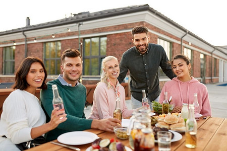 休闲和人的概念-快乐的朋友在屋顶上喝酒，烧烤或晚宴。在屋顶上喝酒或参加烧烤派对的快乐朋友