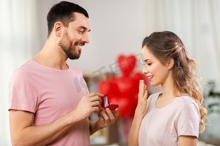 爱情、情侣、求婚和人的概念-快乐的男人把装在小红盒子里的钻石订婚戒指送给家里的女人。