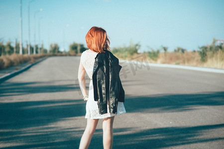 眼睛穿摄影照片_一个穿黑夹克、戴蓝眼镜的红头发女孩走在灰色的路上