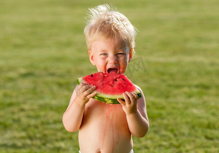 户外蹒跚学步的孩子的肖像。一岁的男婴在花园里吃西瓜片的农村场景。快乐的孩子肮脏的脸。
